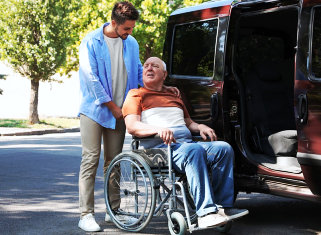 caregiver helping senior man on wheelchair get into the van